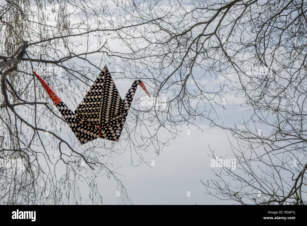 Origami crane in the air, twigs in background Stock Photo