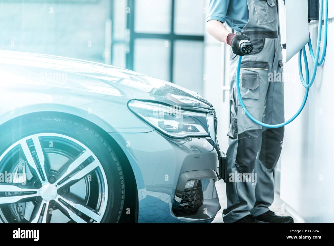 Plug In Hybrid Vehicle and the Charging Station. Worker Preparing To Hookup Modern Vehicle to the Power Outlet. Stock Photo