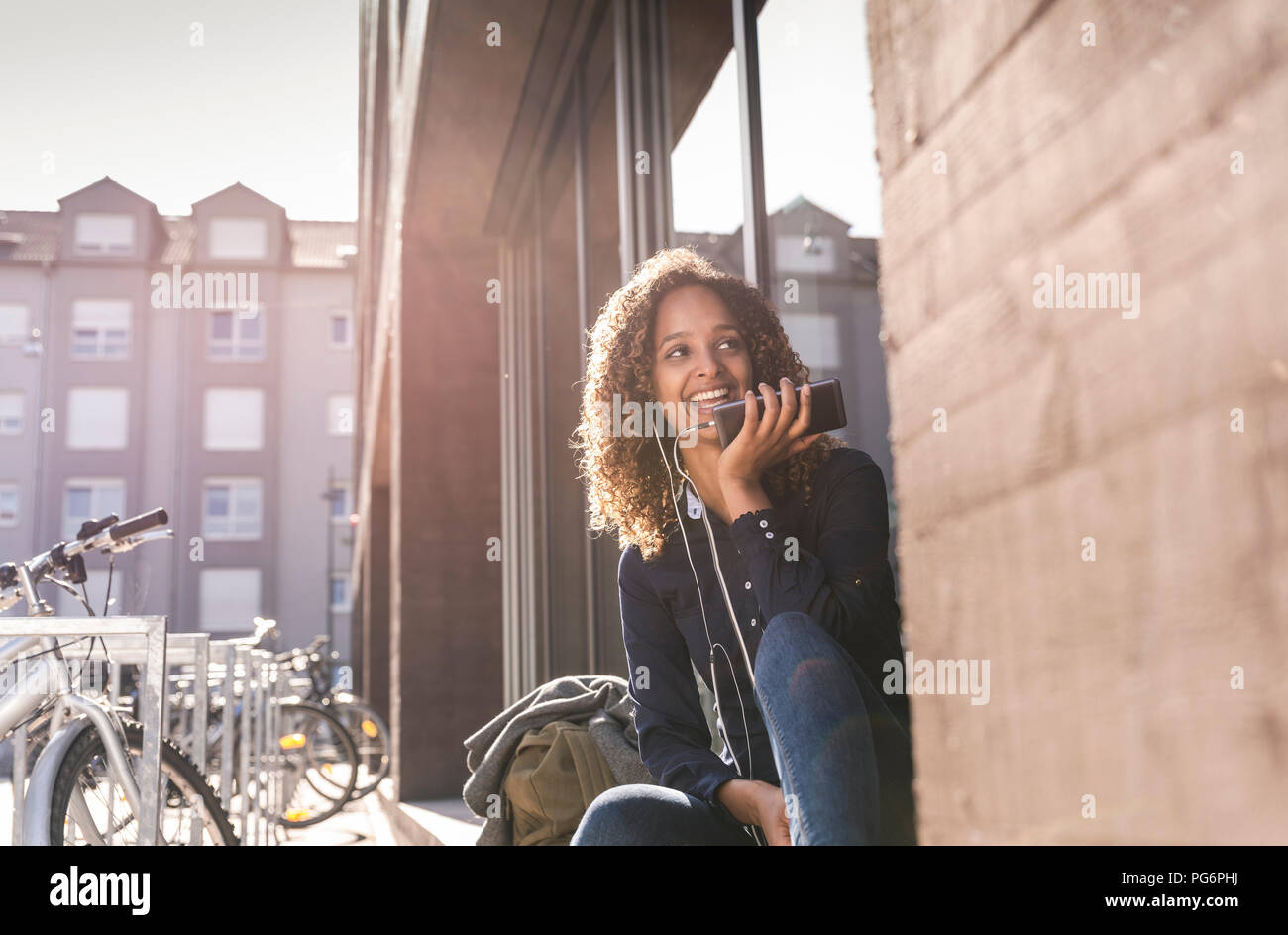 Young woman sitting in front of window in the city, using smartphone Stock Photo