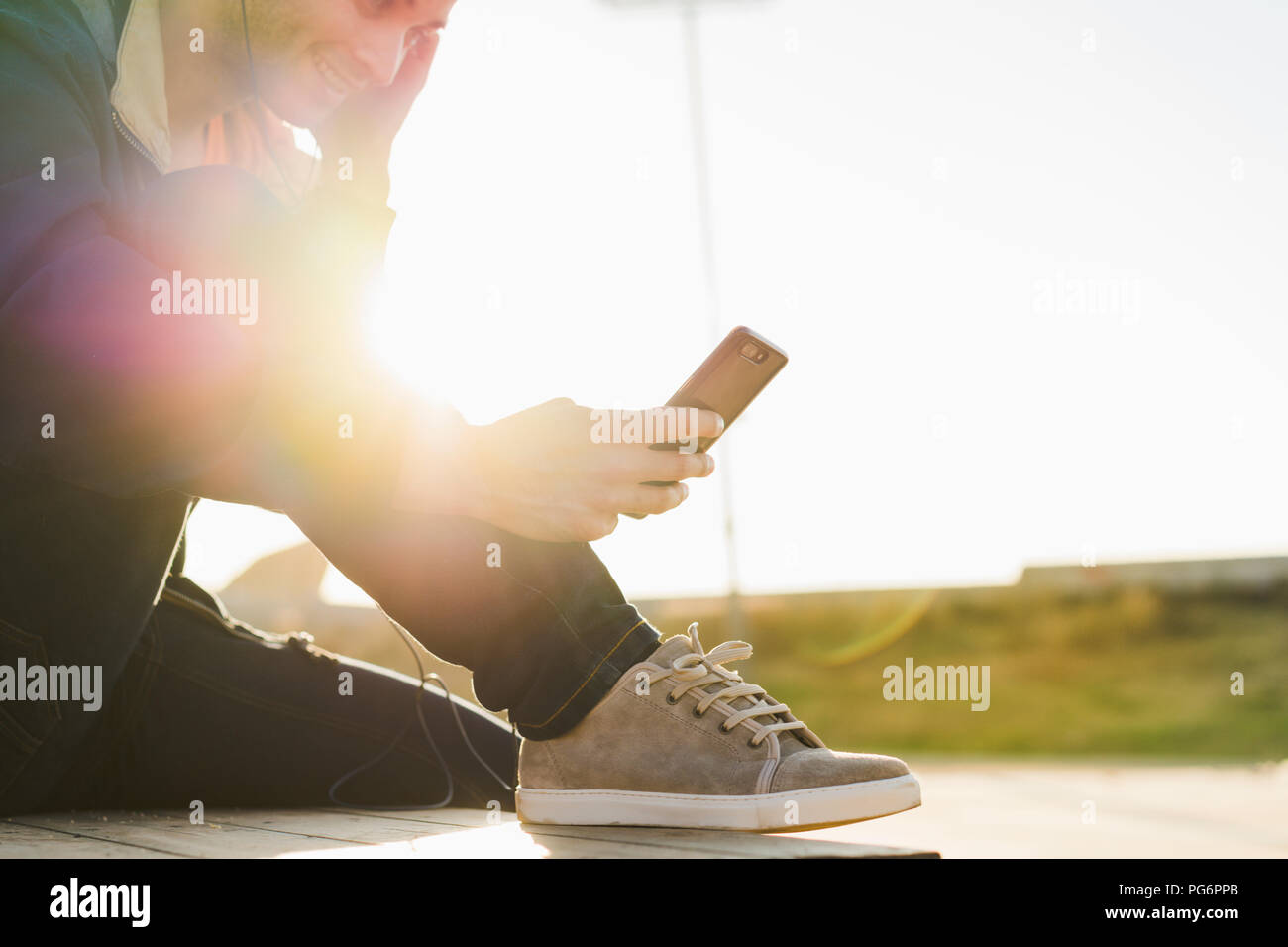 Man with headphones sitting on wood stack, using smartphone Stock Photo