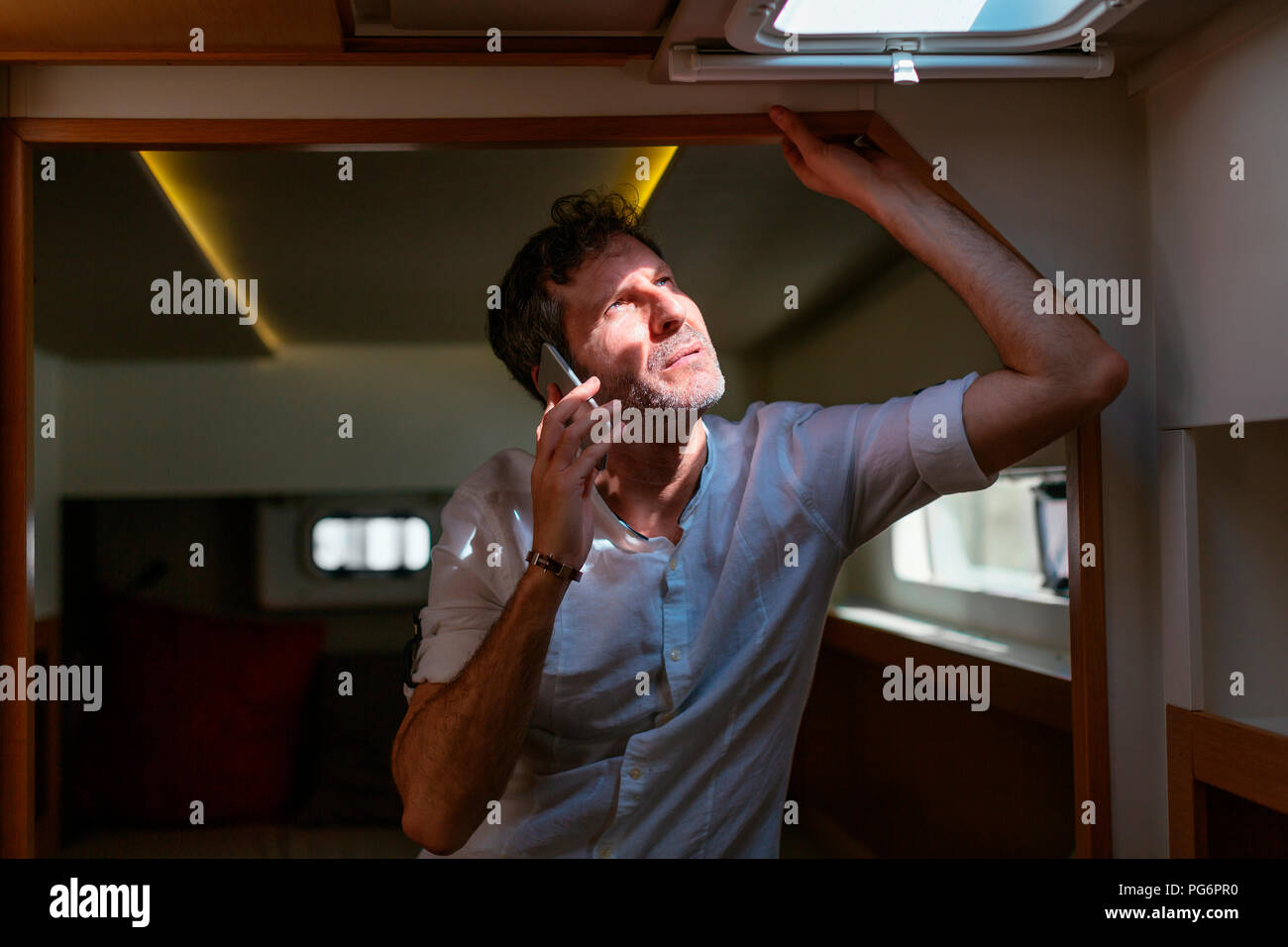 Mature man standing in catamaran cabin, looking up , using smartphone Stock Photo