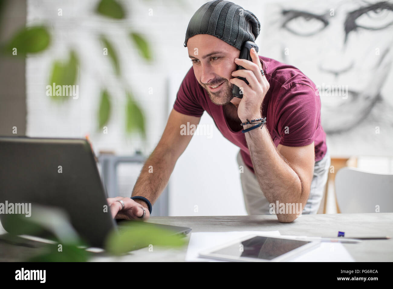 Artist using laptop and cell phone in studio Stock Photo