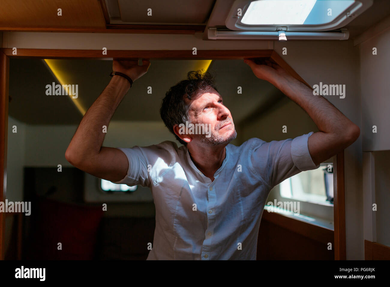 Mature man standing in catamaran cabin, looking up through hatch Stock Photo