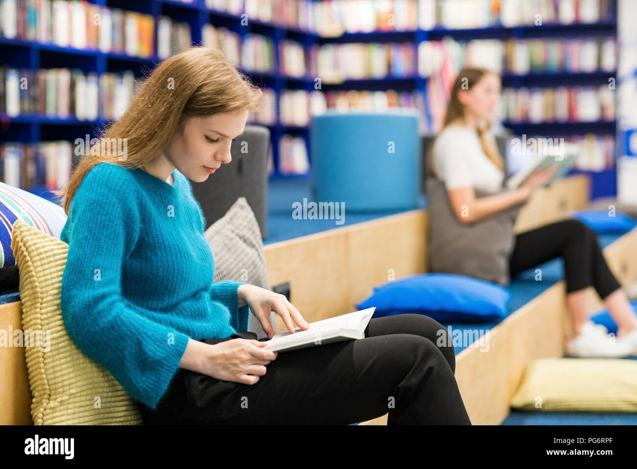 Teenage girls sitting in a public library reading book Stock Photo