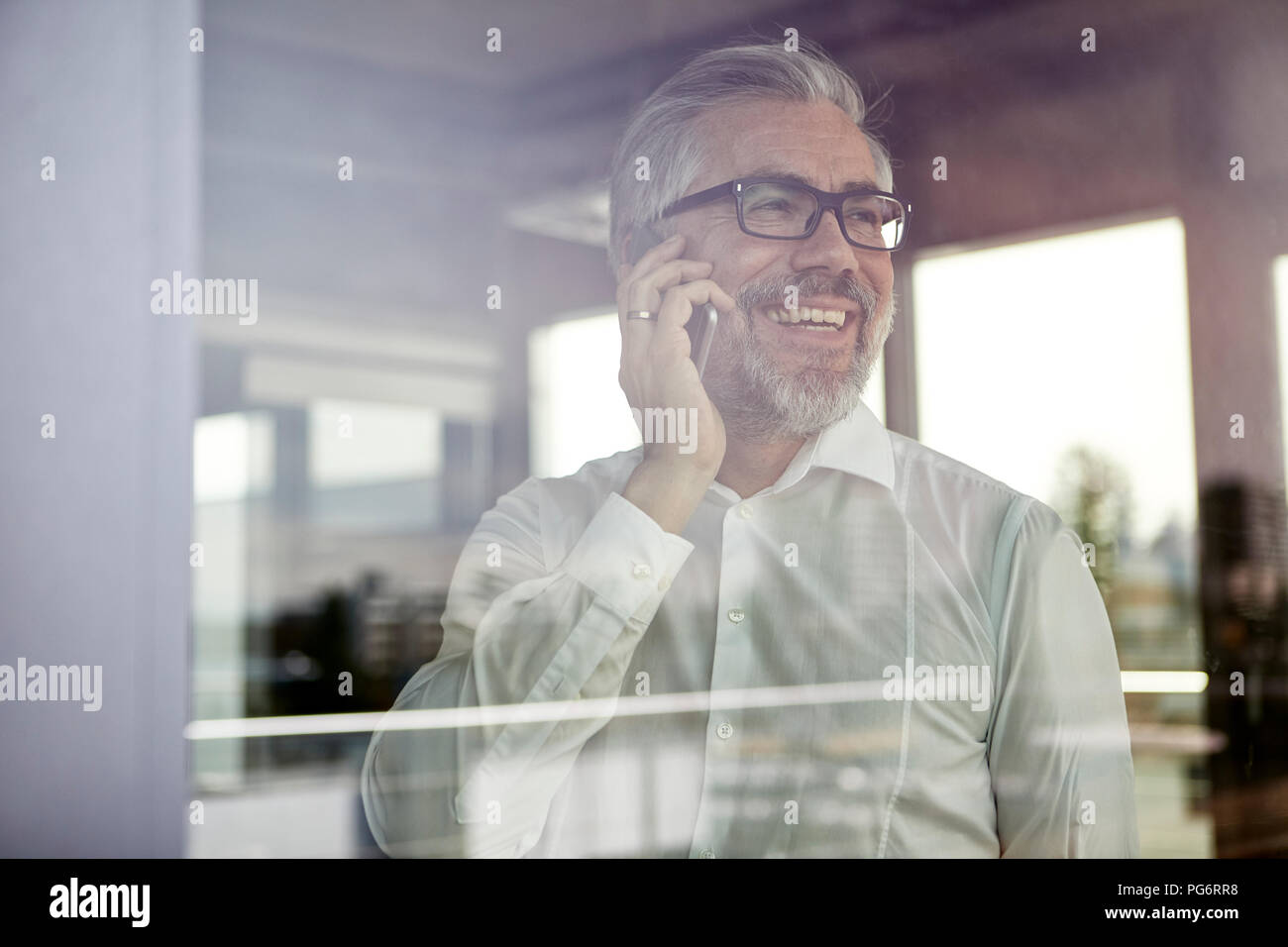 Laughing businessman at the window talking on cell phone Stock Photo