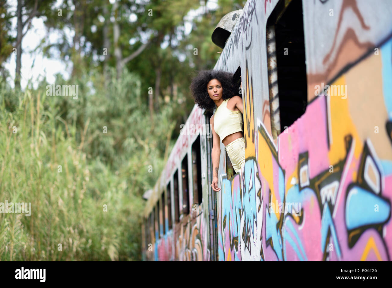 Fashionable young woman leaning out of window of an abandoned and destroyed old train Stock Photo