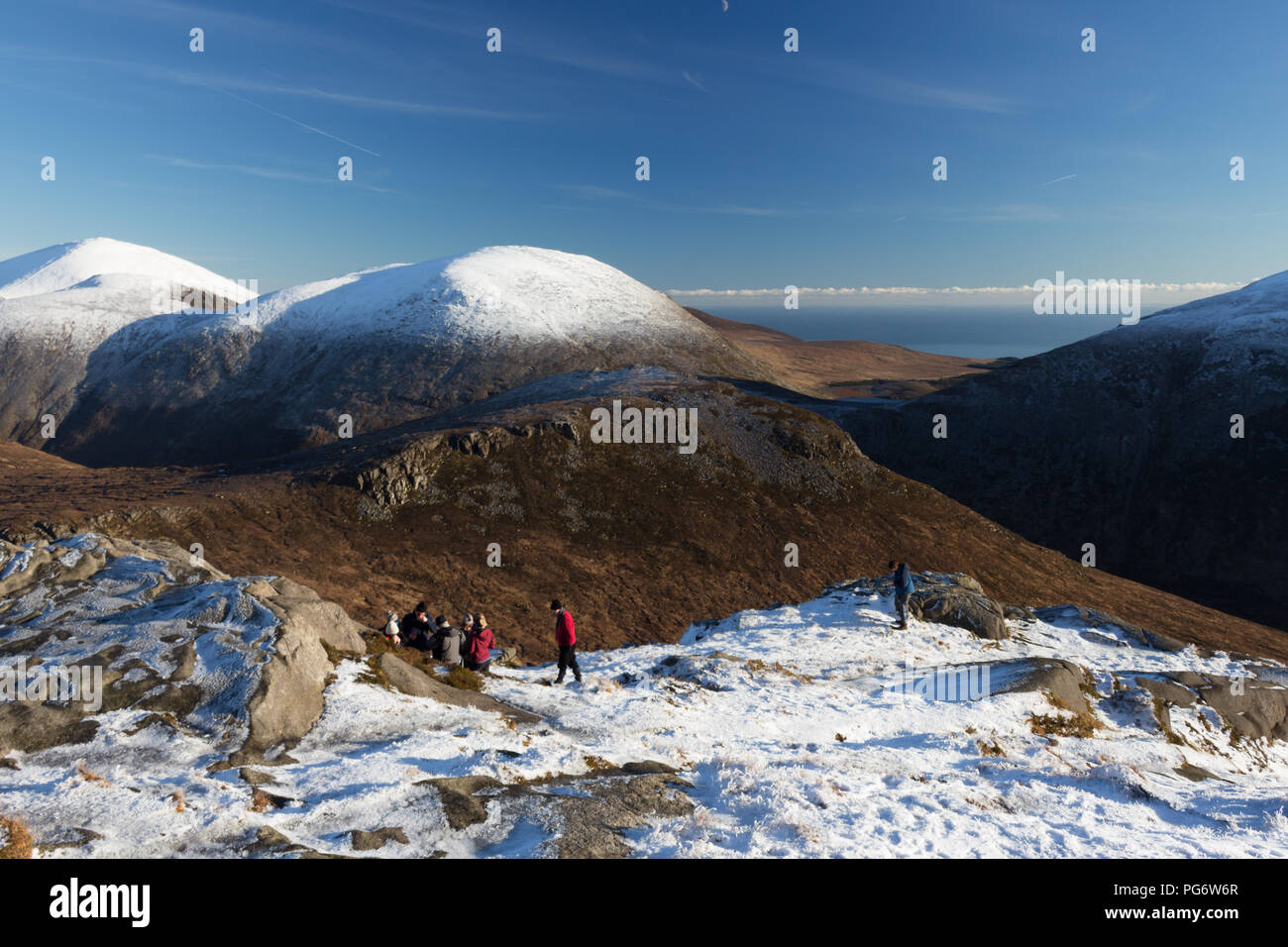 Group of winter hillwalkers enjoying a rest on Doan mountain. Views to Ben Crom directly in front and snowcapped Lamagan behind. Slieve Donard on left. Stock Photo