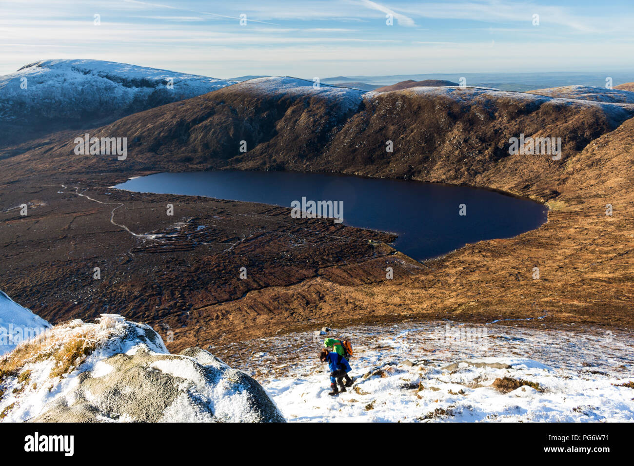 Two hillwalkers descending steep ground in snow on Doan Mountain towards Lough Shannagh with Carn Mountain and Slieve Muck behind. Stock Photo