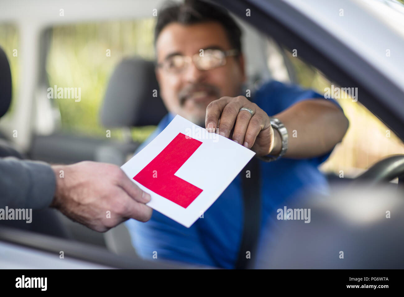 Driving instructor holding L sign in car Stock Photo
