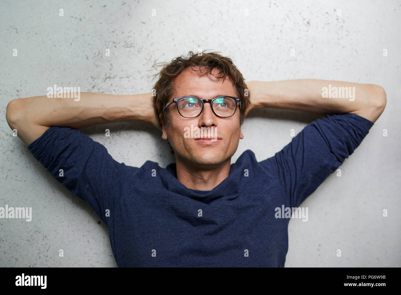 Portrait of man with hands behind head wearing glasses Stock Photo
