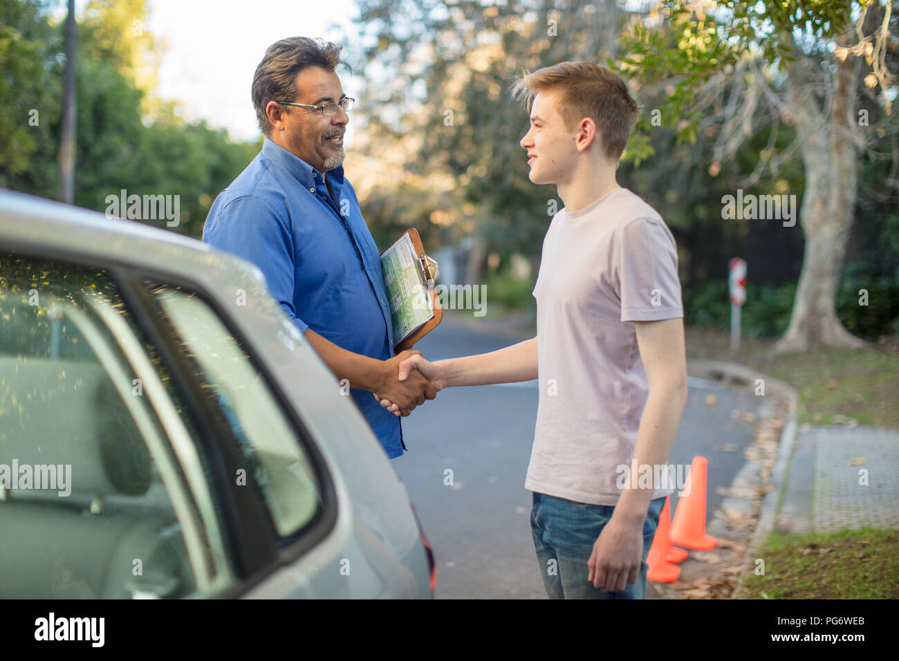 Learner driver and instructor shaking hands at car Stock Photo