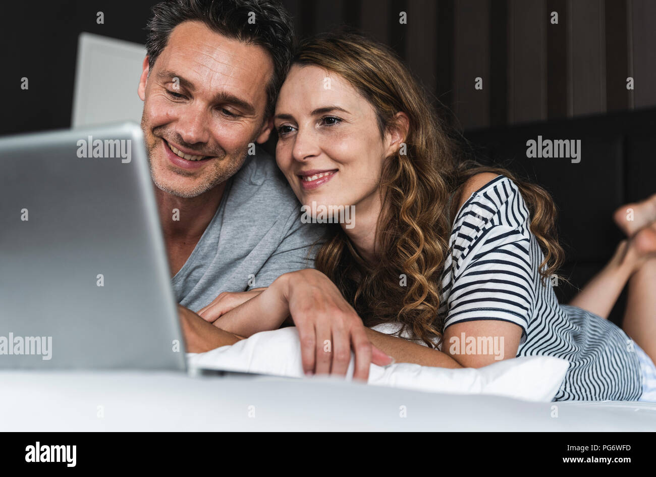 Happy couple lying on bed at home looking at laptop Stock Photo - Alamy