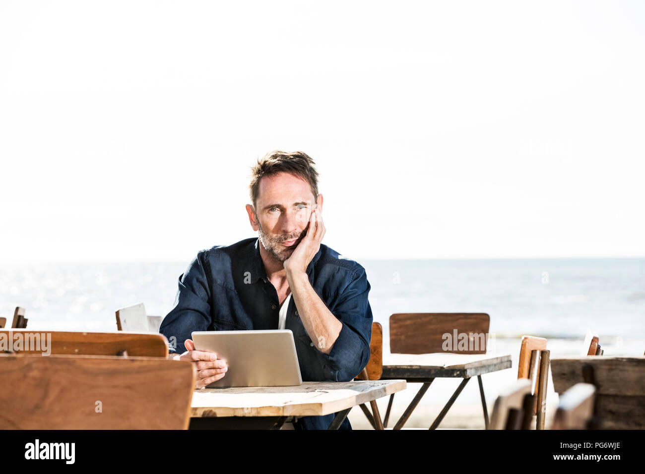 Man with tablet sitting in a cafe on the beach Stock Photo