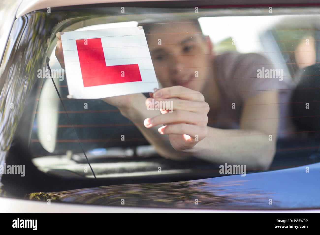 Learner driver placing letter L on rear window of car Stock Photo