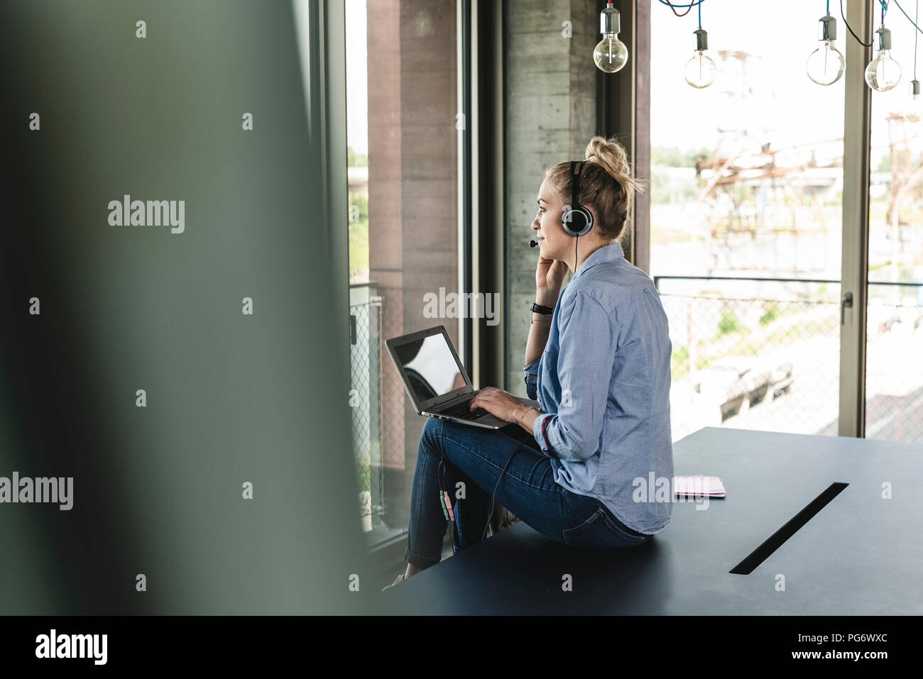 Young businesswoman sitting at desk, making a call, using headset and laptop Stock Photo