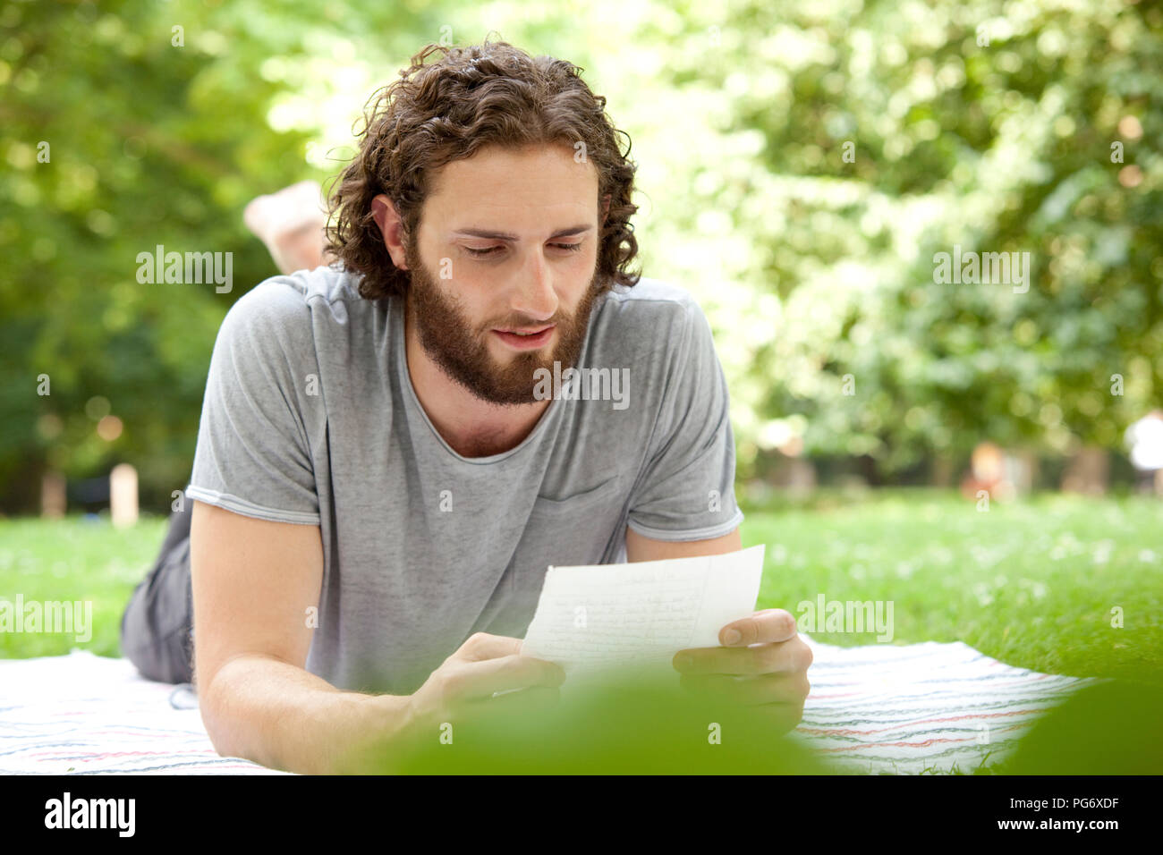 Man lying on blanket in a park reading a letter Stock Photo