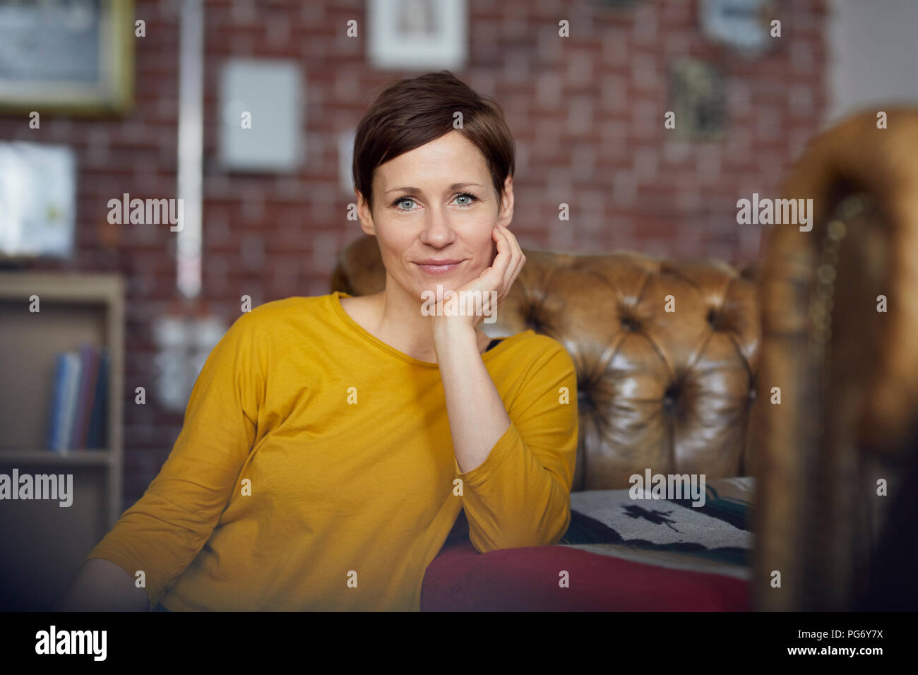 Attractive woman sitting at home with hand on chin Stock Photo - Alamy