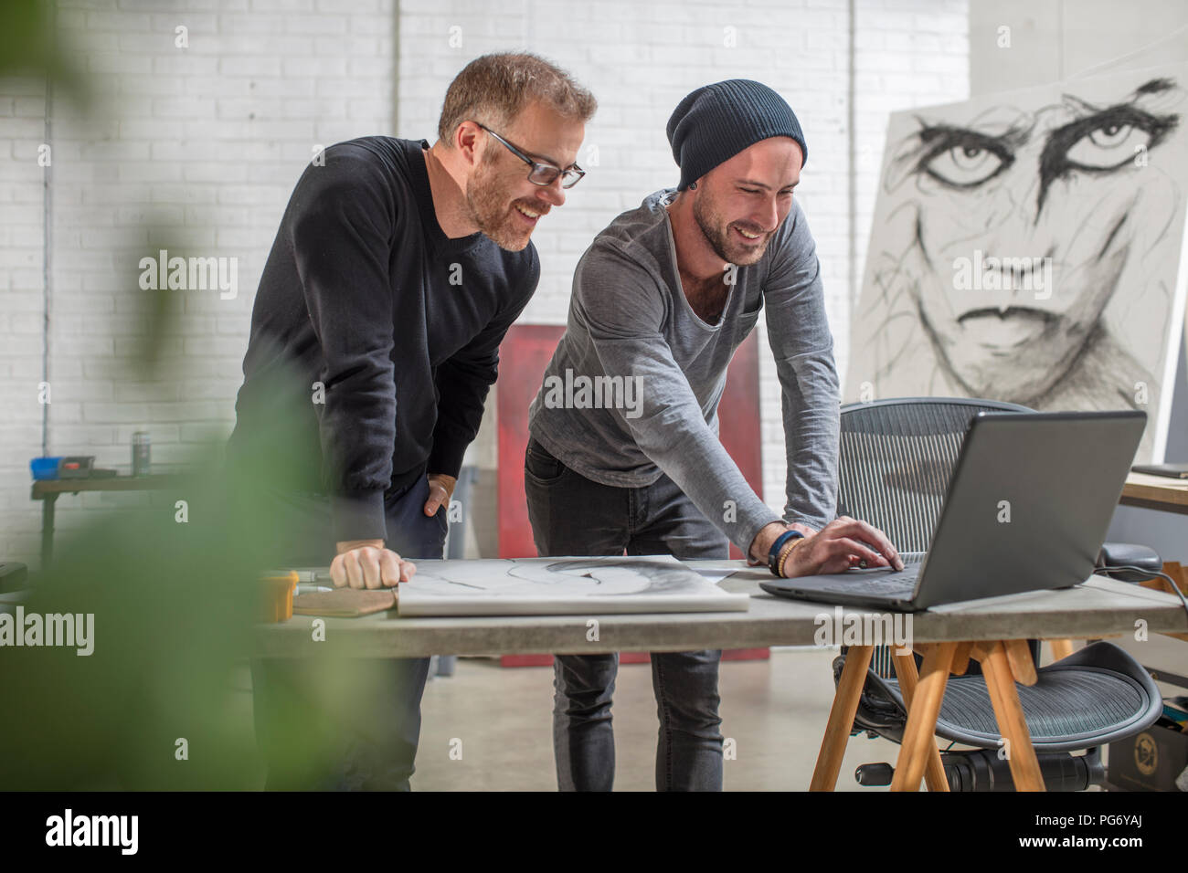 Smiling artist using laptop with man in studio Stock Photo