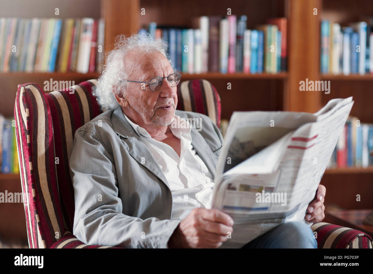 Senior man sitting in library, reading newpaper Stock Photo