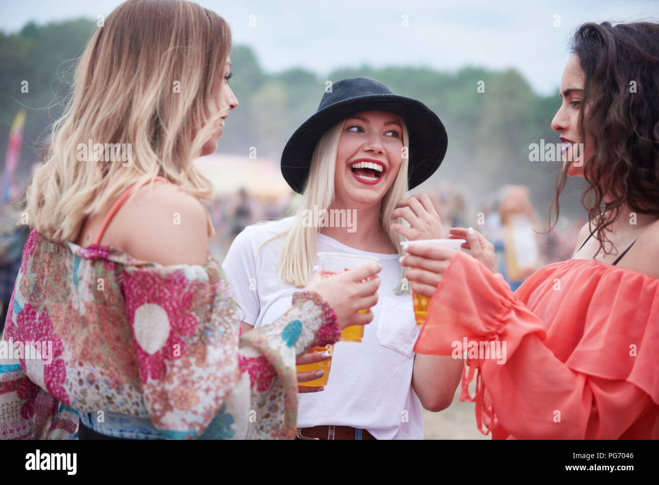 Friends drinking juice and sitting on meadow during music festival Stock Photo