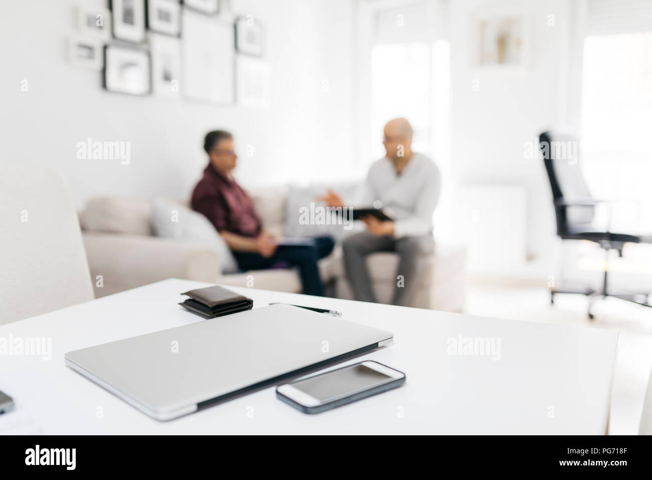 Cell phone, laptop and wallet on table at home with two men talking in ...