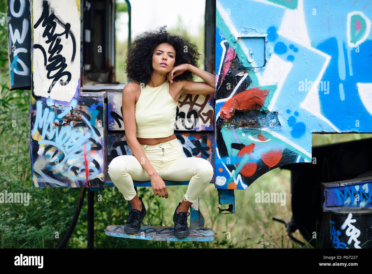Portrait of fashionable young woman sitting on steps of an abandoned and destroyed old train Stock Photo