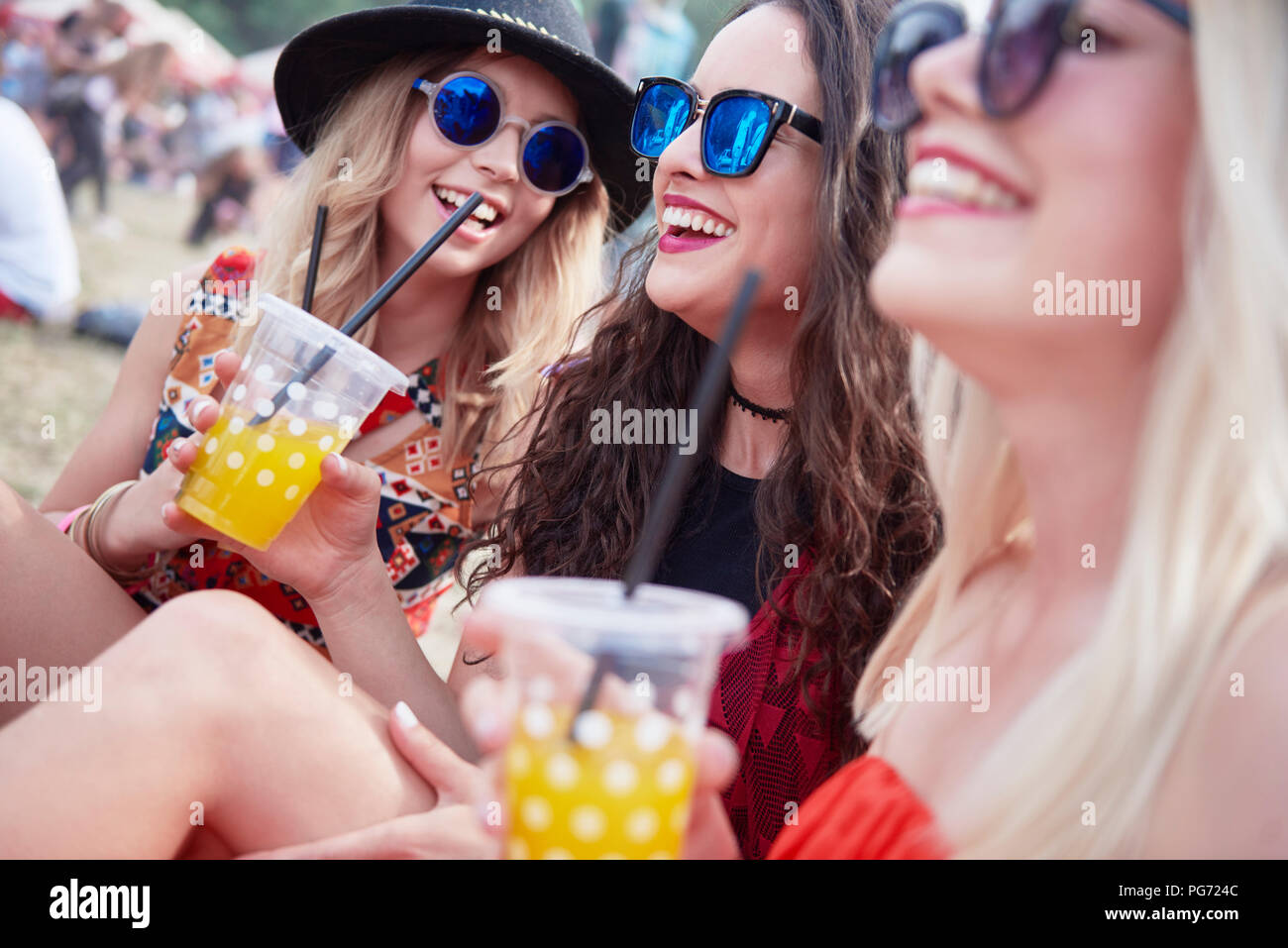 Friends drinking juice and sitting on meadow during music festival Stock Photo