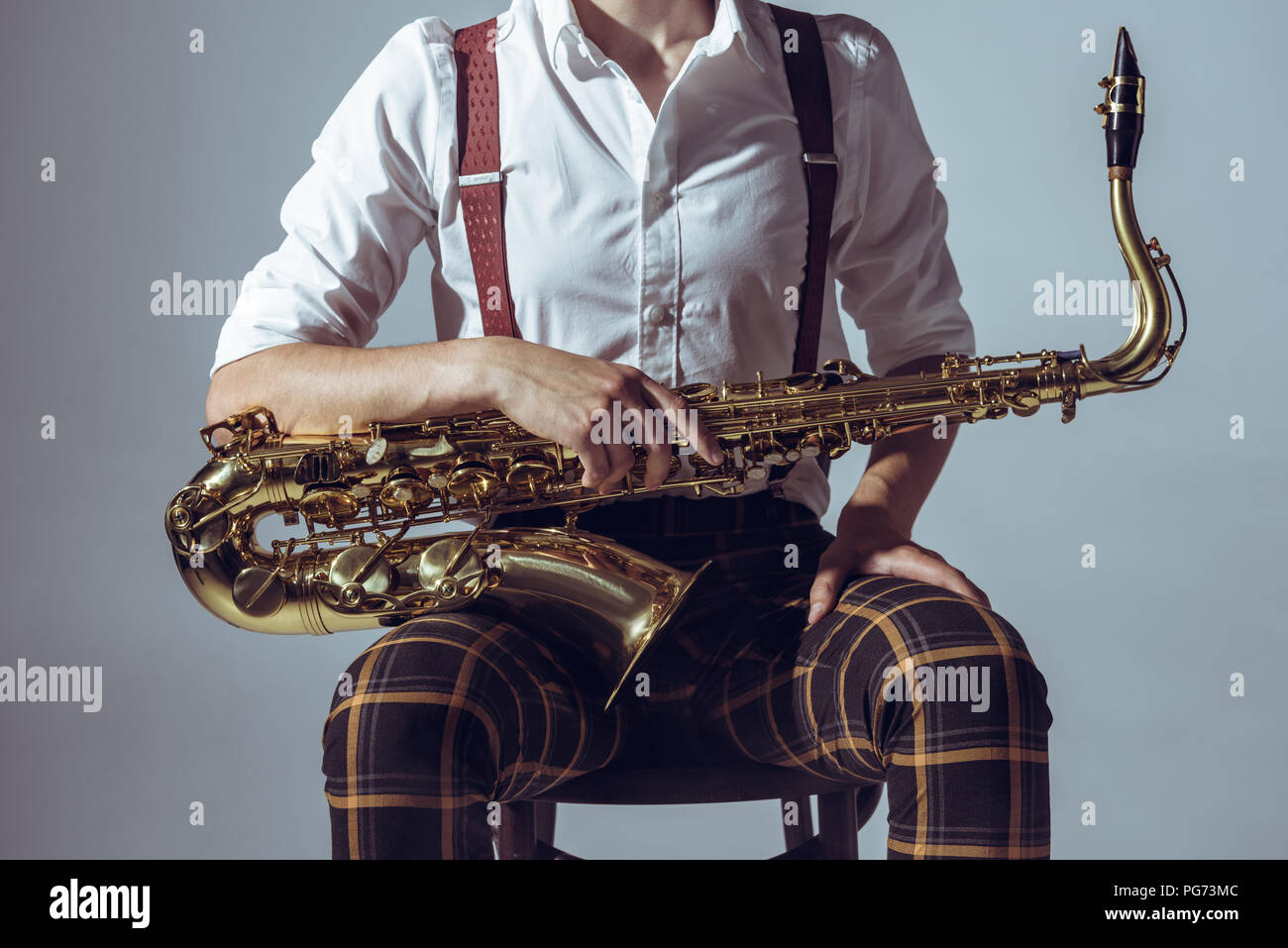 cropped shot of young musician sitting on chair and holding saxophone isolated on grey Stock Photo