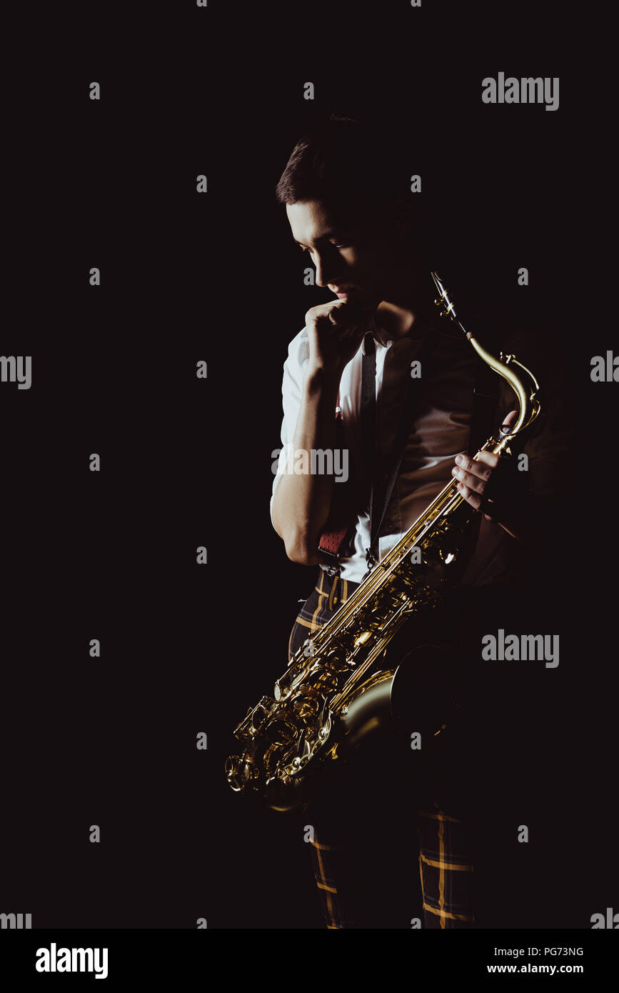pensive young musician holding saxophone isolated on black Stock Photo