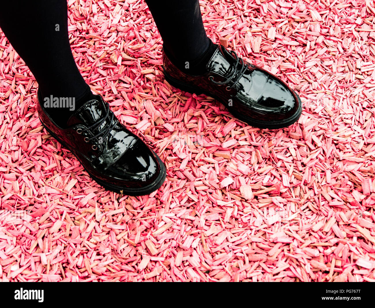 Girl's shiny black shoes on pink woodchip ground Stock Photo - Alamy