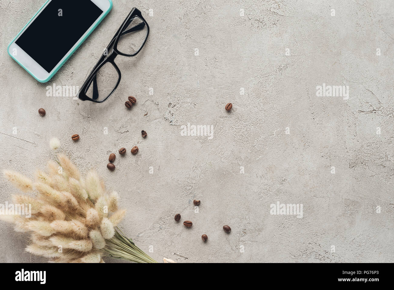 top view of smartphone with blank screen with eyeglasses, spilled coffee beans and lagurus ovatus bouquet on concrete surface Stock Photo