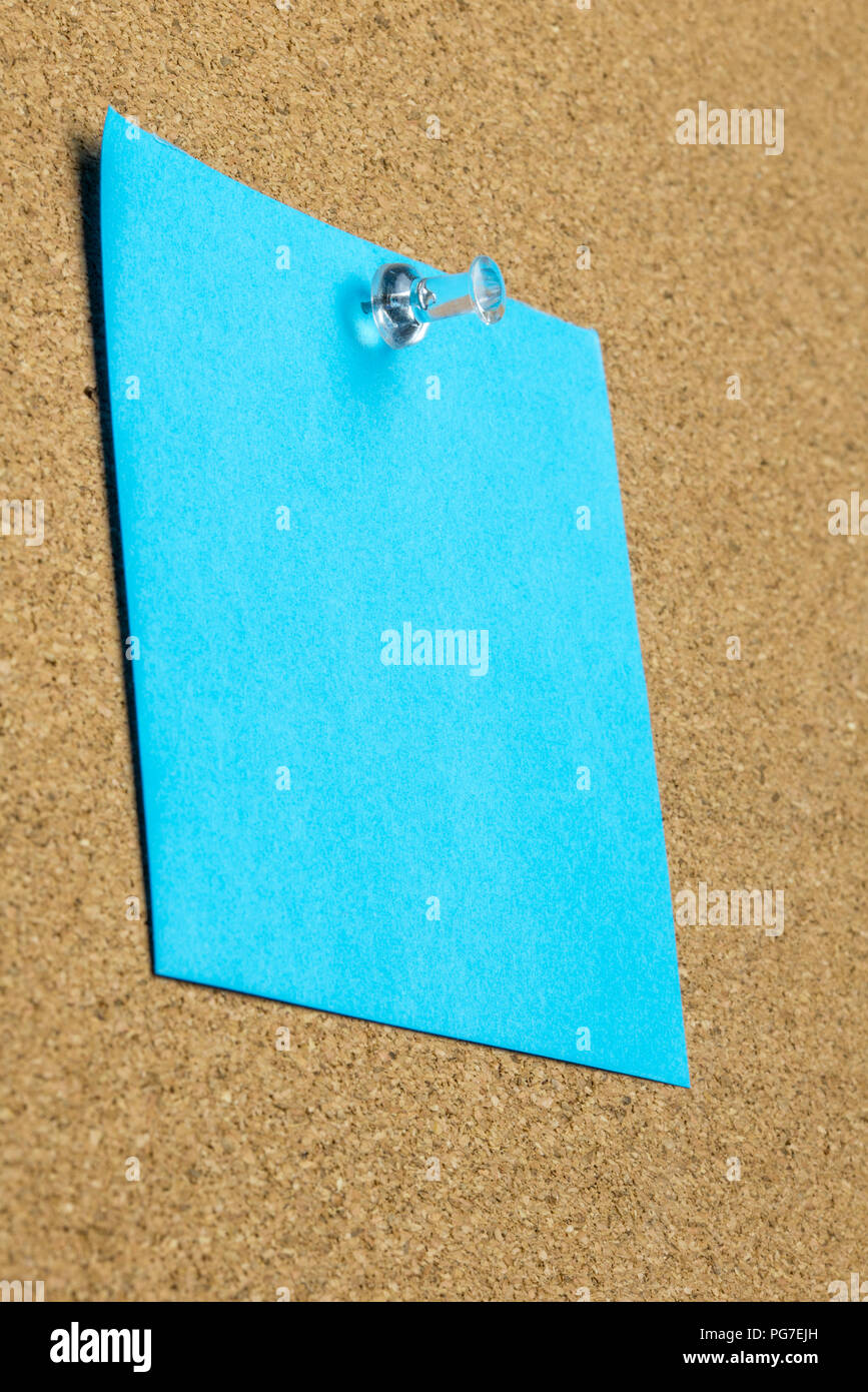 Blank sheet of blue paper with copyspace pinned up on a cork bulletin board with a thumb tack viewed at an oblique angle from below. Stock Photo