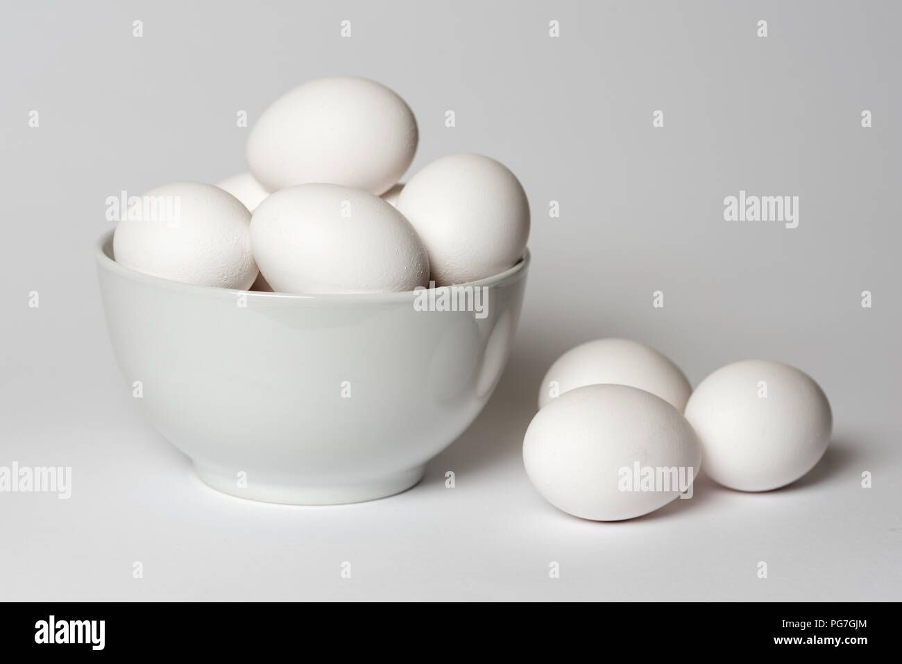 White eggs in a china bowl with three lying alongside all on a white background Stock Photo