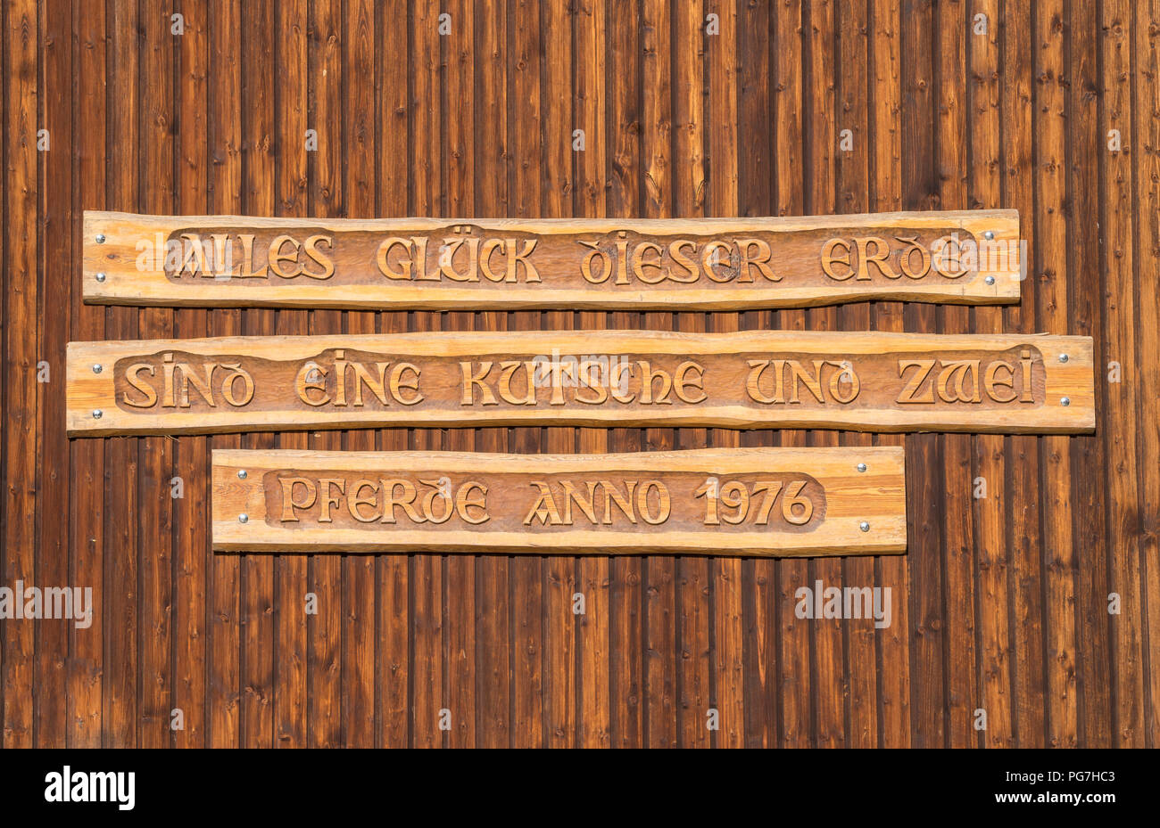 German quote on a big wooden door which means: ALL LUCK OF THIS WORLD BELONGS TO THE CARRIAGE AND ITS TWO HORSES, ANNO 1976 Stock Photo