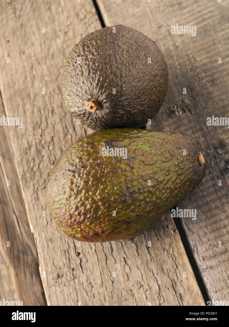 Two avocados on a rustic wooden kitchen table Stock Photo