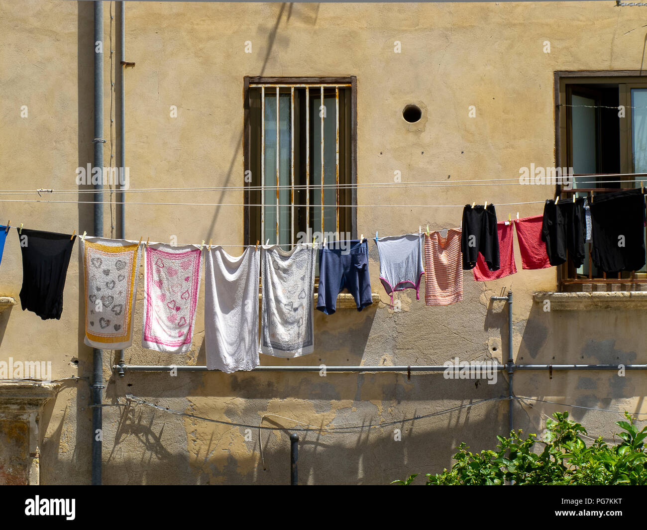 long row of colorful clothes hung to dry at the window of a building, in the popular district of an Italian city Stock Photo