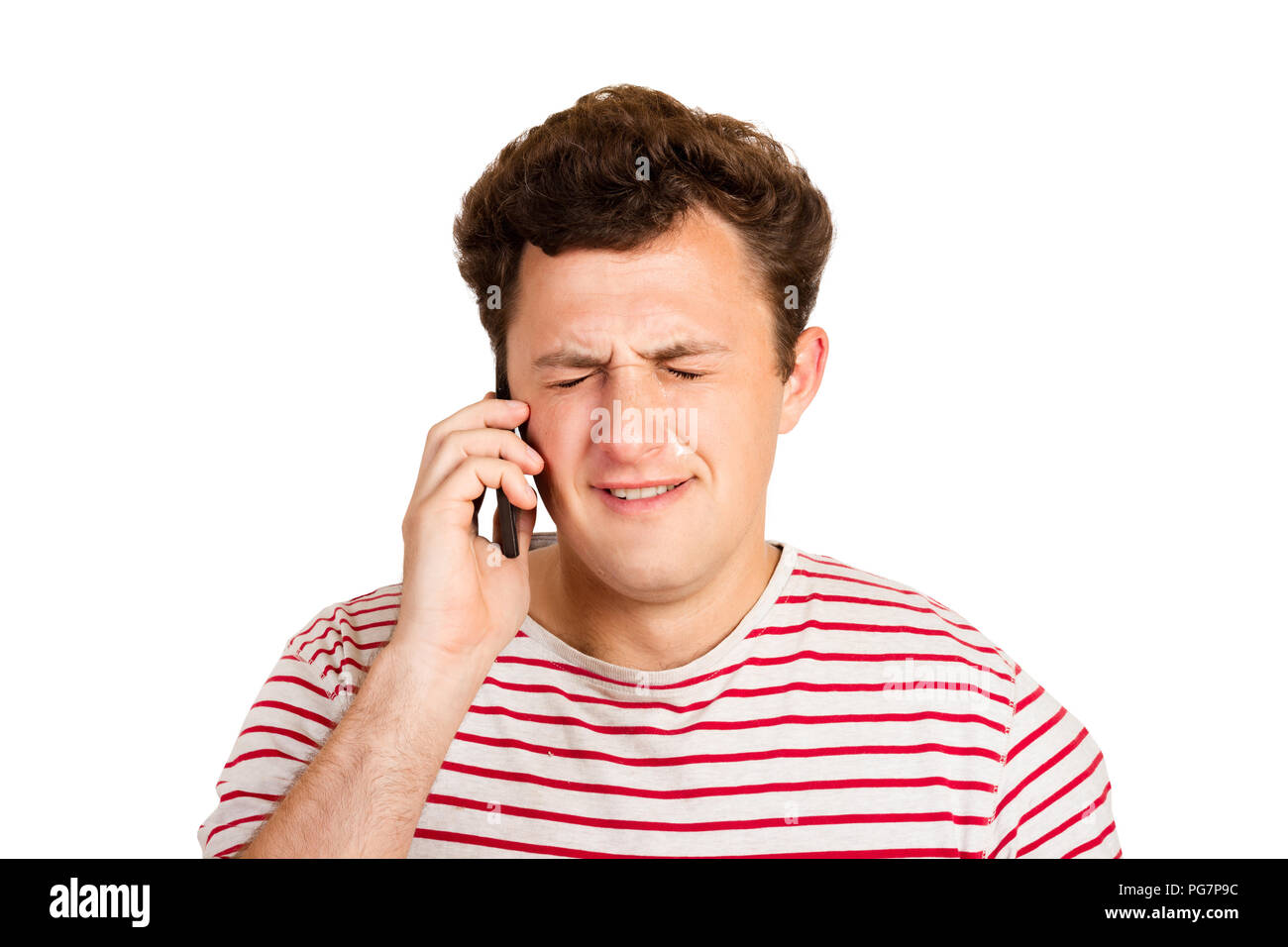 A young man cries about bad news by closing his eyes and thinking about the problem that he gets on his phone. emotional man isolated on white backgro Stock Photo