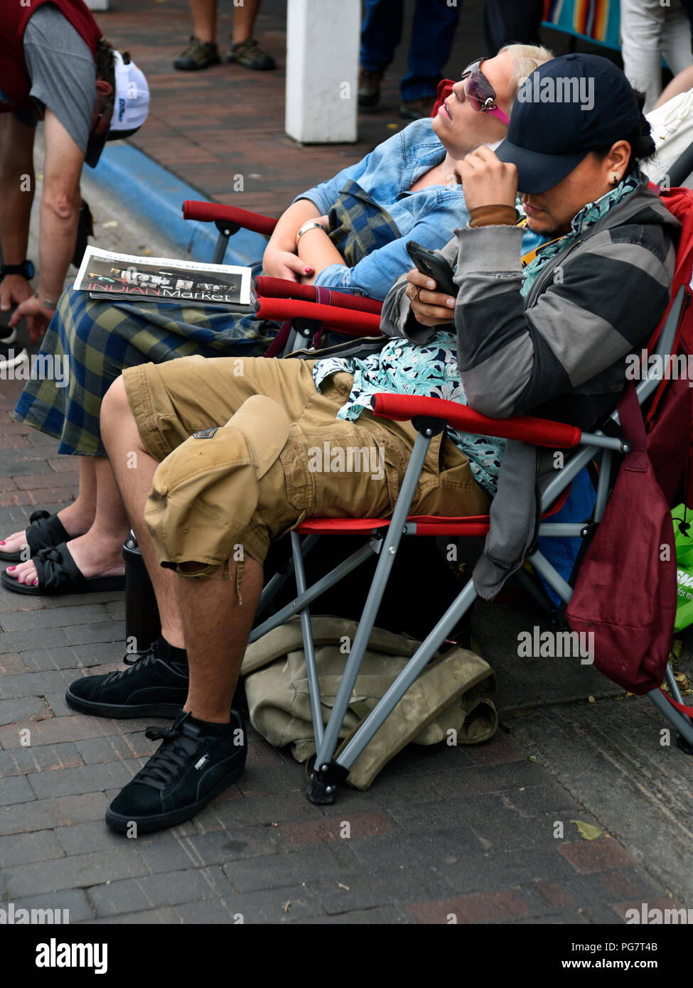Two exhibitors, one sleeping and the other using his smartphone, sit near their booth at an outdoor art show in Santa Fe, New Mexico. Stock Photo