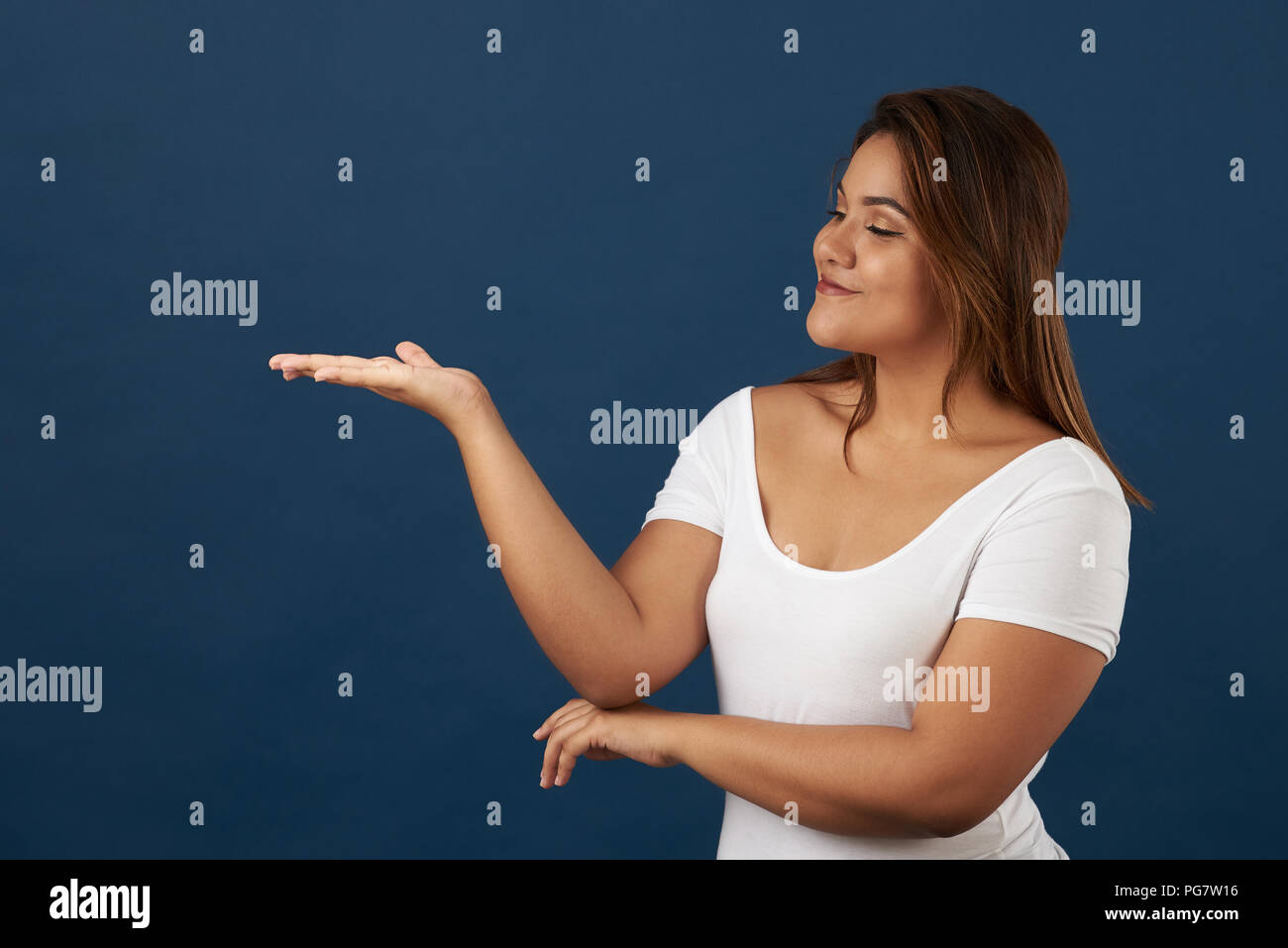 Young woman look on open hand palm in blue studio background Stock Photo