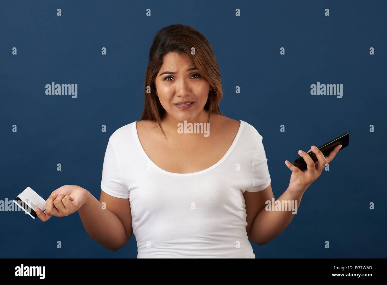 Upset woman with smartphone and credit card isolated on blue studio background Stock Photo