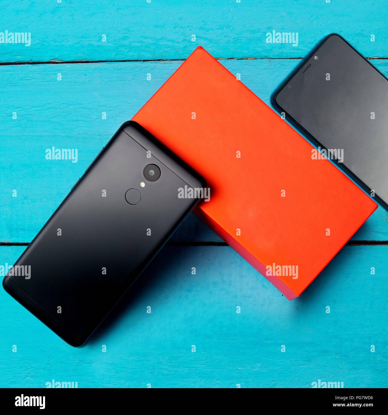 Two smartphones on top of a wooden board, blue background and orange box Stock Photo