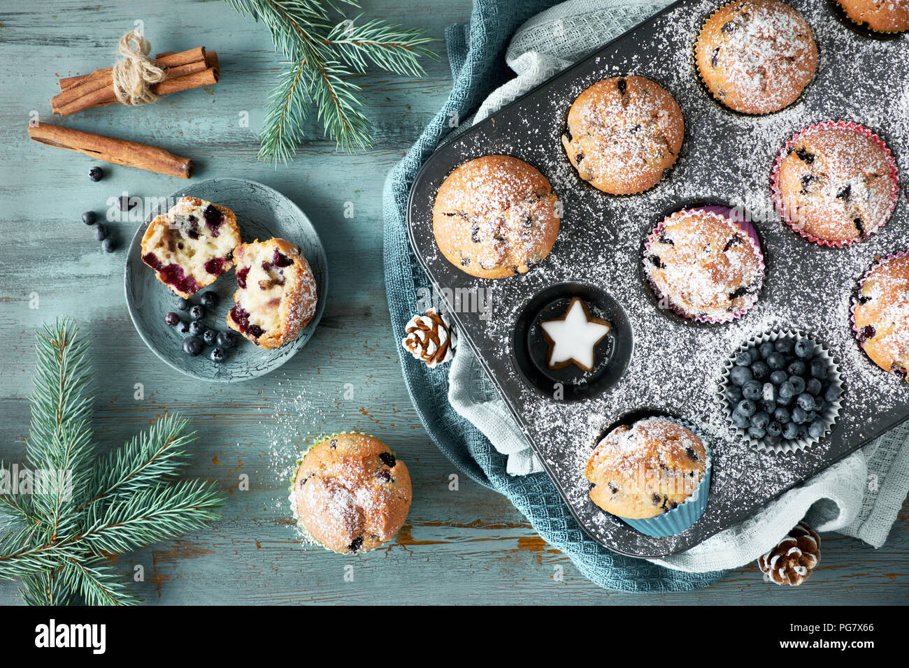 Blueberry muffins with sugar icing in a baking tray with Christmas decorations around, flat lay, view from above Stock Photo