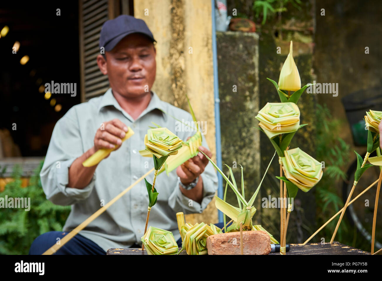 A talented street artist making and selling palm leaf roses in the streets of Hoi An, Vietnam. Stock Photo