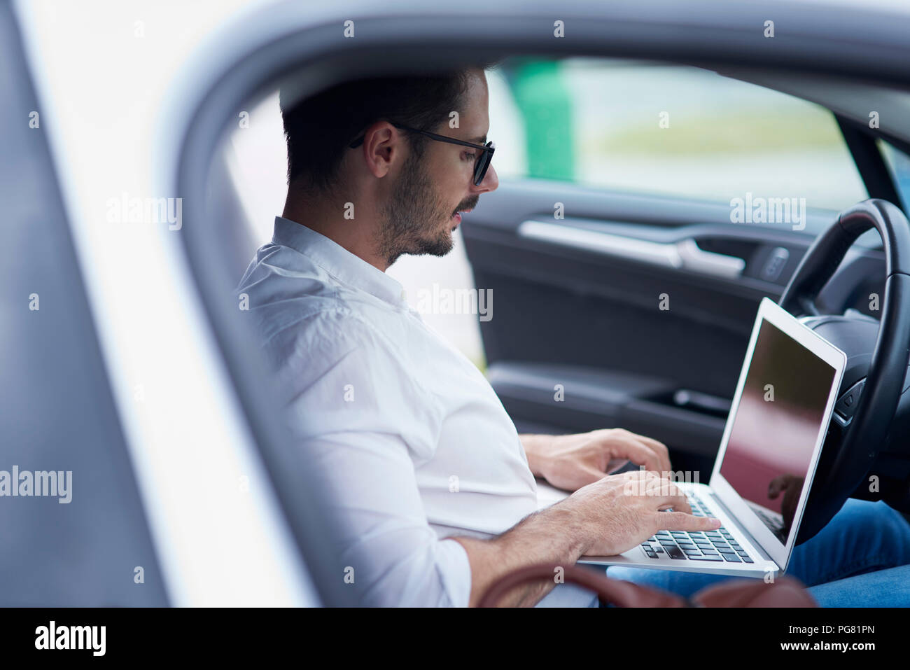 Businessman sitting in car working on laptop Stock Photo