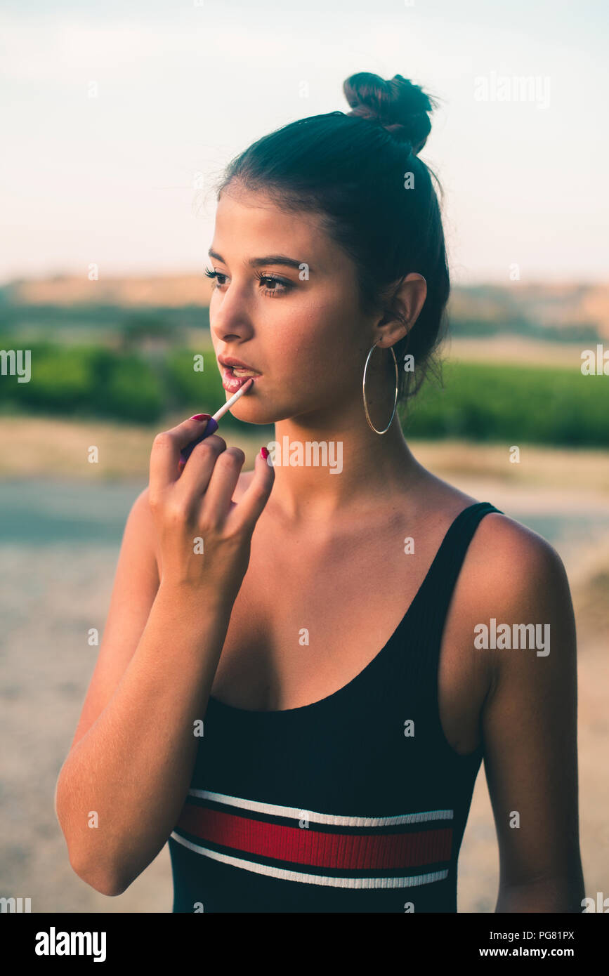 Portrait of teenage girl in nature applying lip gloss Stock Photo