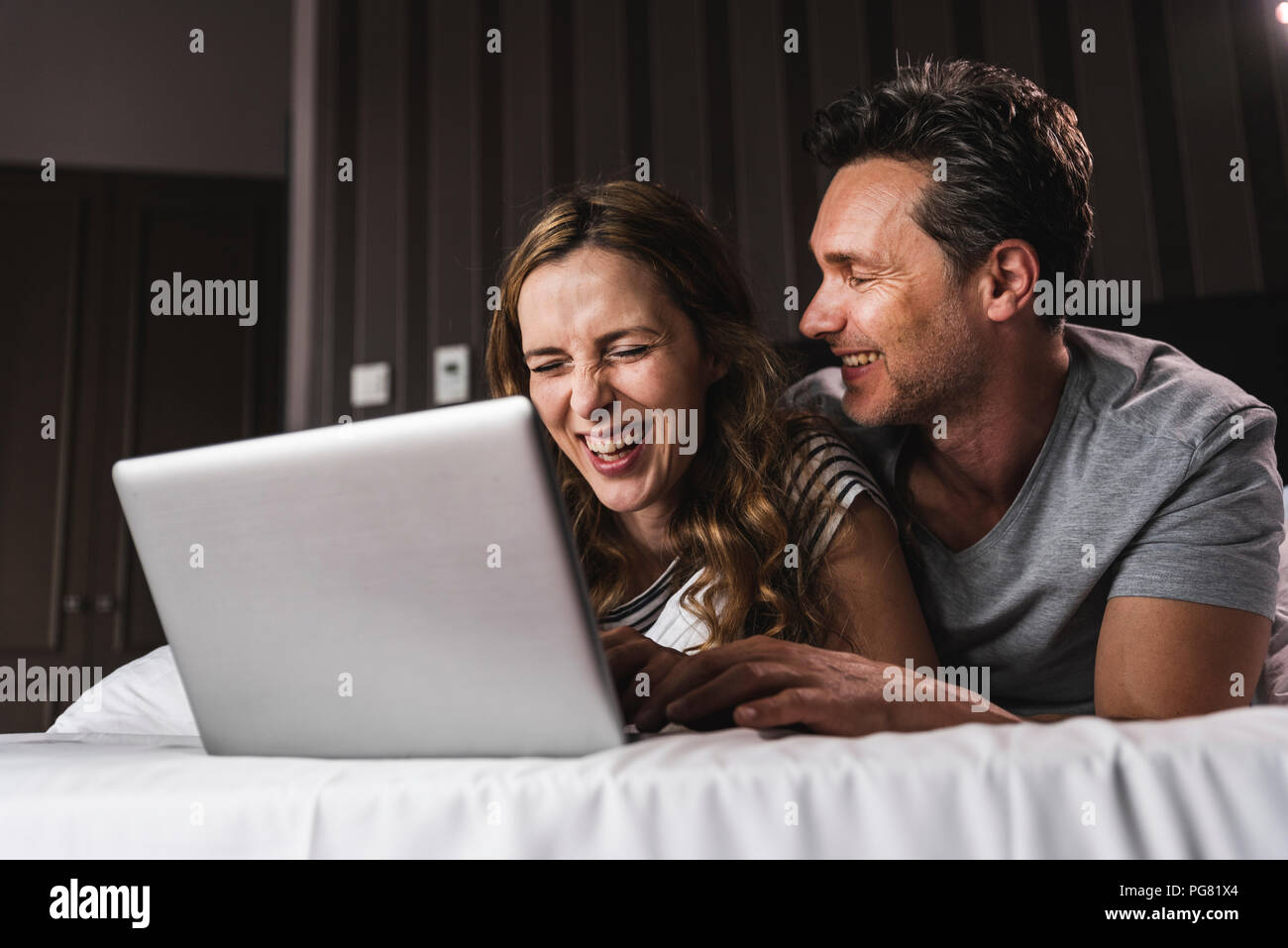 Happy couple lying on bed at home having fun with laptop Stock Photo ...