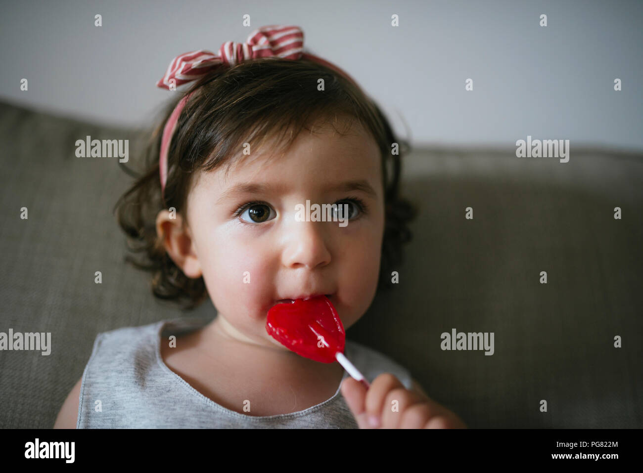 Cute baby girl eating a heart shaped lollipop at home Stock Photo