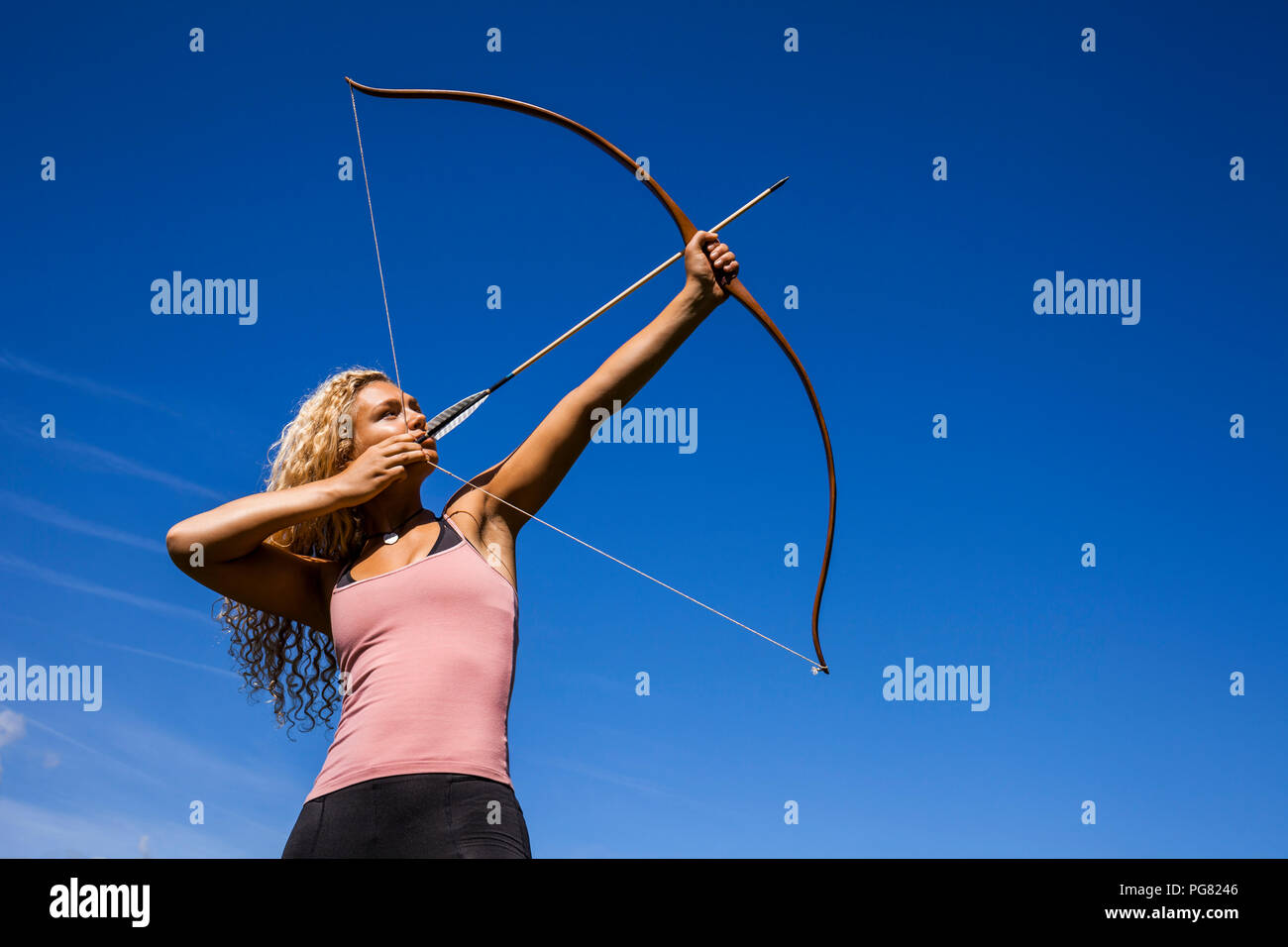 Archeress aiming with bow against blue sky Stock Photo