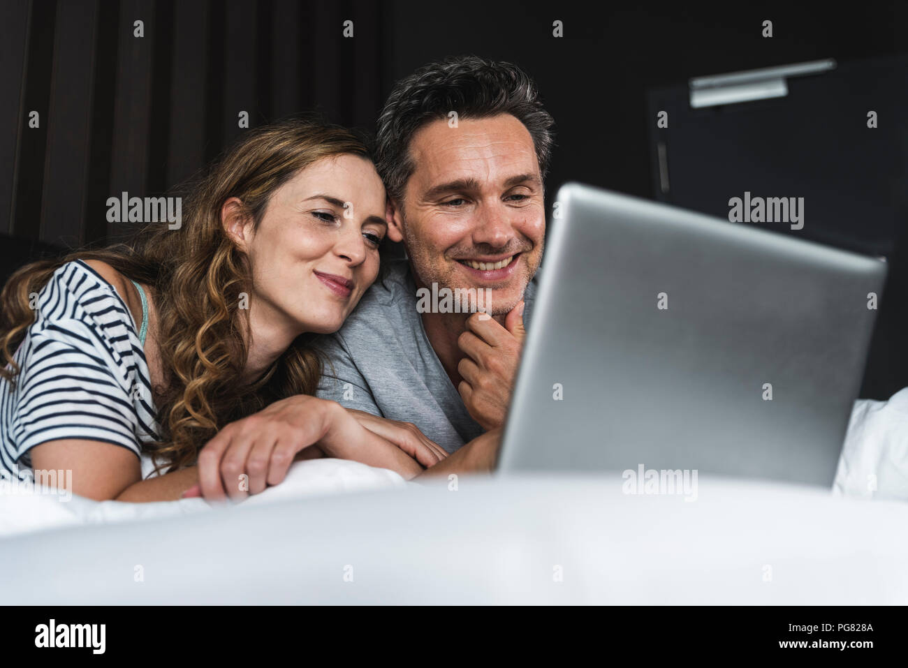 Happy couple lying on bed at home looking at laptop Stock Photo - Alamy