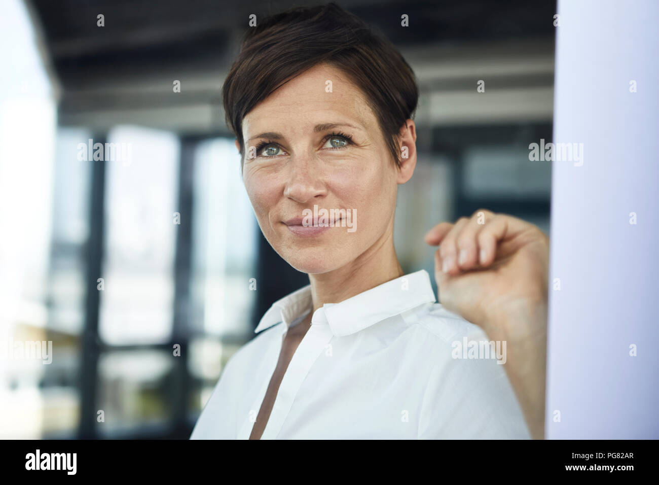 Portrait of smiling businesswoman in office looking out of window Stock Photo